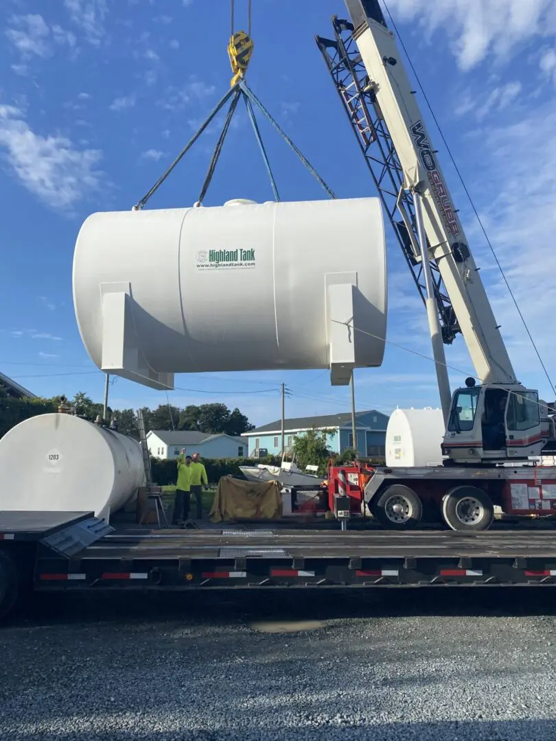 A crane lifting a large tank on to the back of a truck.